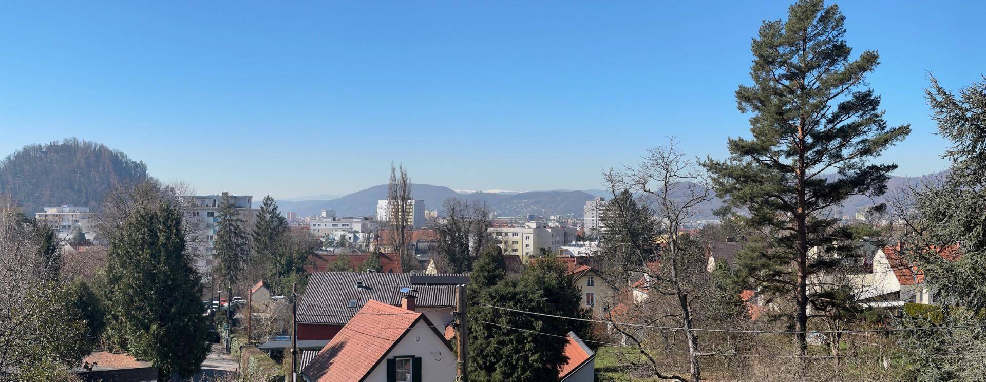 Panoramablick über die Stadt und die umliegende grüne Landschaft mit Bergen im Hintergrund.
