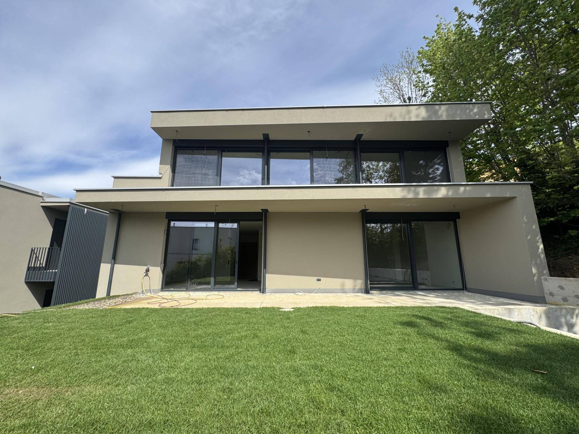 Rückansicht der modernen Villa mit weitläufiger Rasenfläche und großen Fensterfronten.