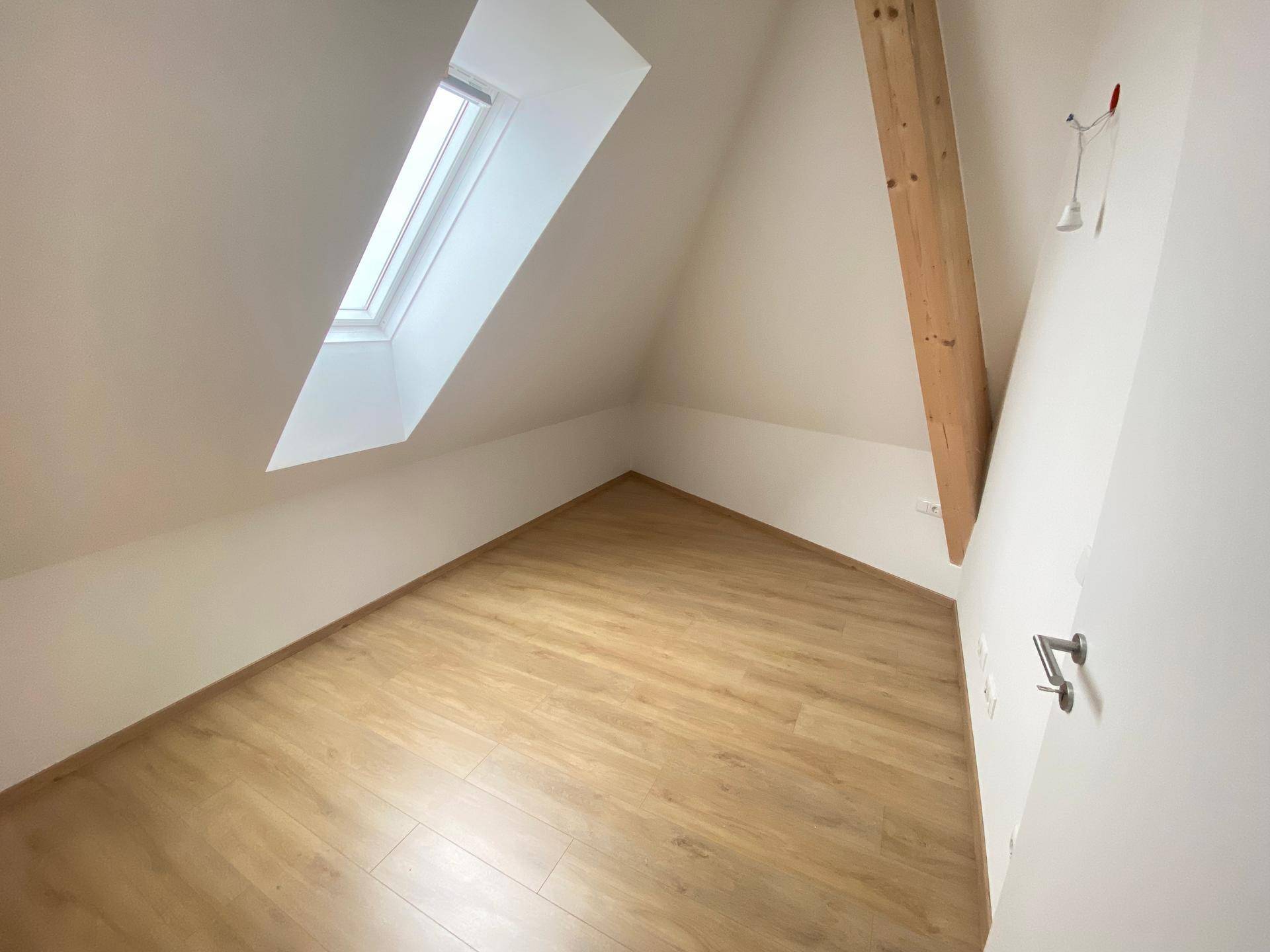 Gemütliches Dachzimmer mit sichtbarem Holzbalken, Laminatboden und einem Dachfenster für natürliches Licht.