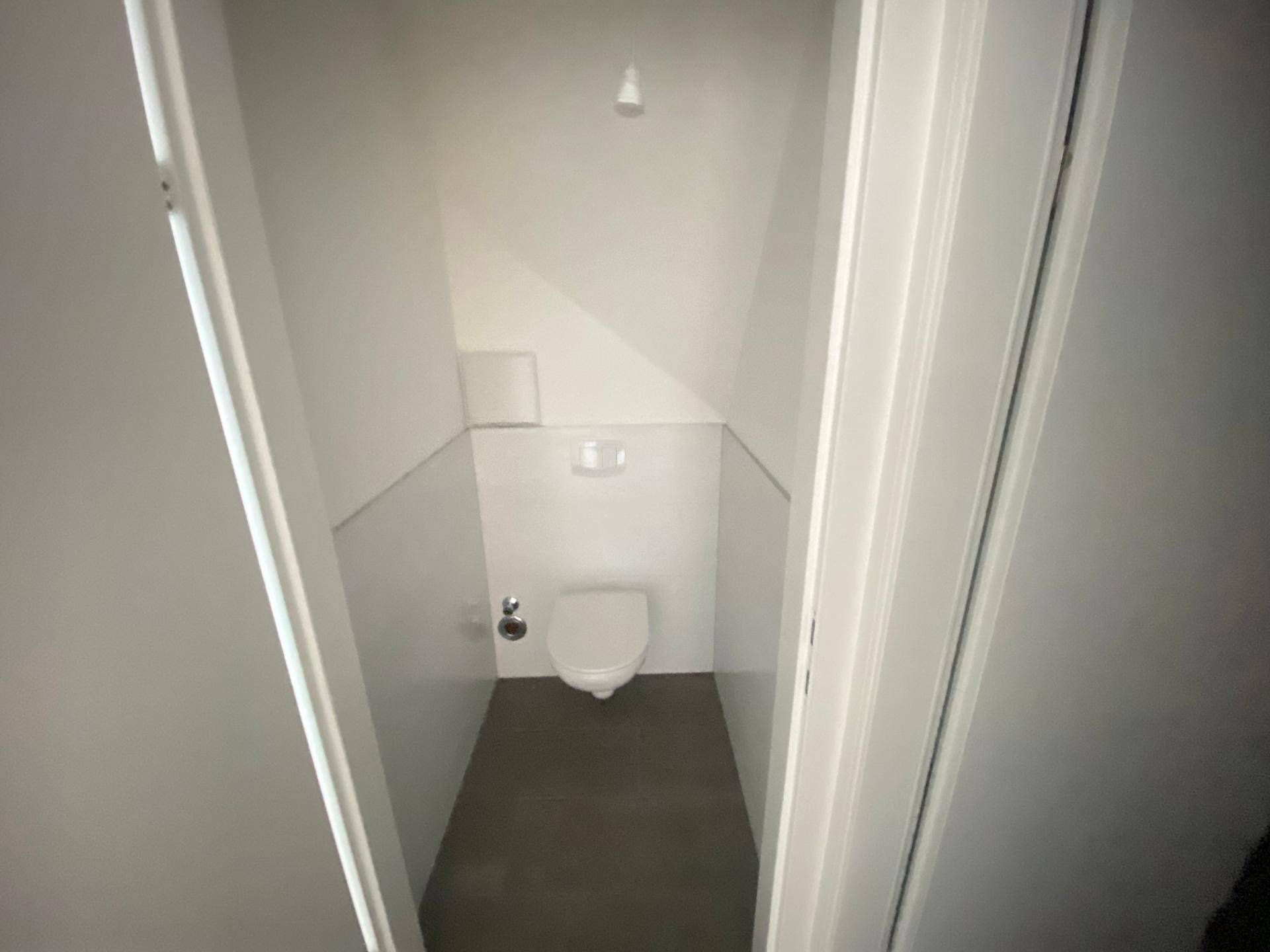 Kleines WC mit wandhängender Toilette und Fliesen, geschickt unter der Dachschräge platziert.