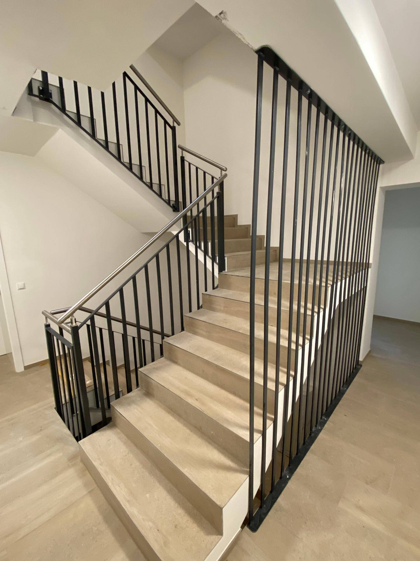 Modernes Treppenhaus mit eleganten Metallgeländern und hellen Fliesenstufen, die zu den oberen Etagen führen.