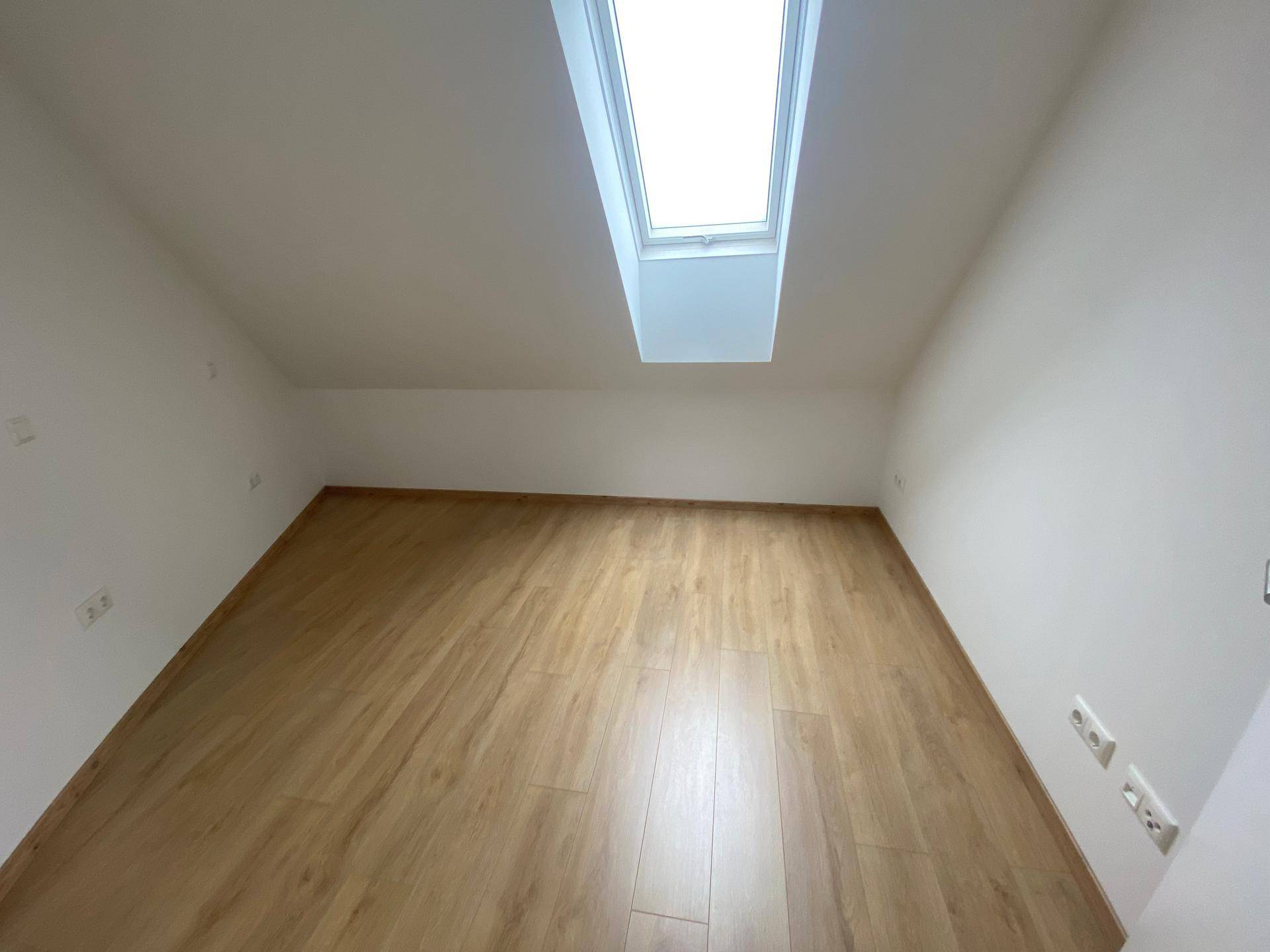 Dachgeschosszimmer mit hellem Laminatboden und großem Dachfenster, das viel Tageslicht hereinlässt.