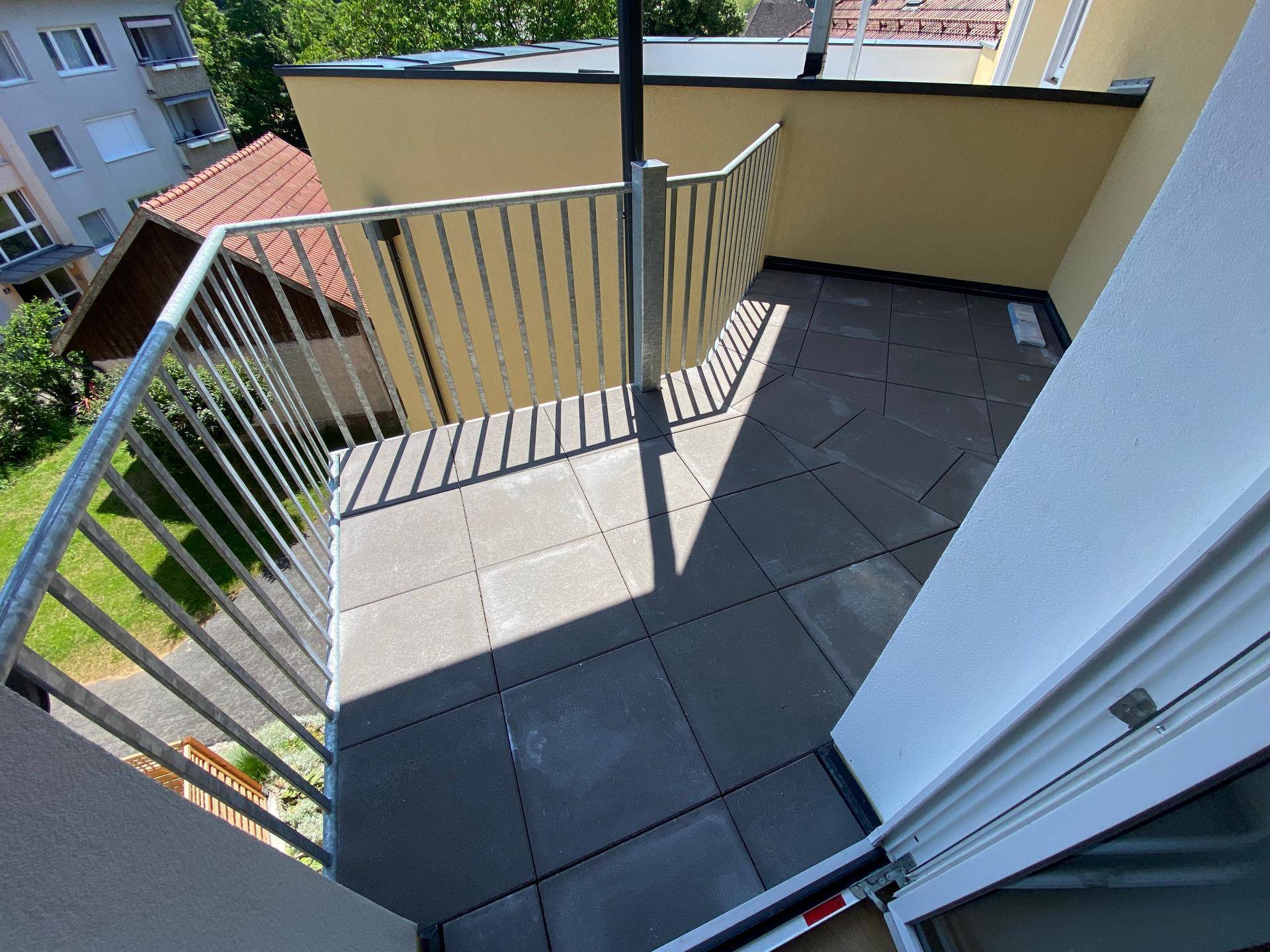 Heller Balkon mit Fliesenboden und Metallgeländer, bietet einen Blick auf die Umgebung und Grünflächen.