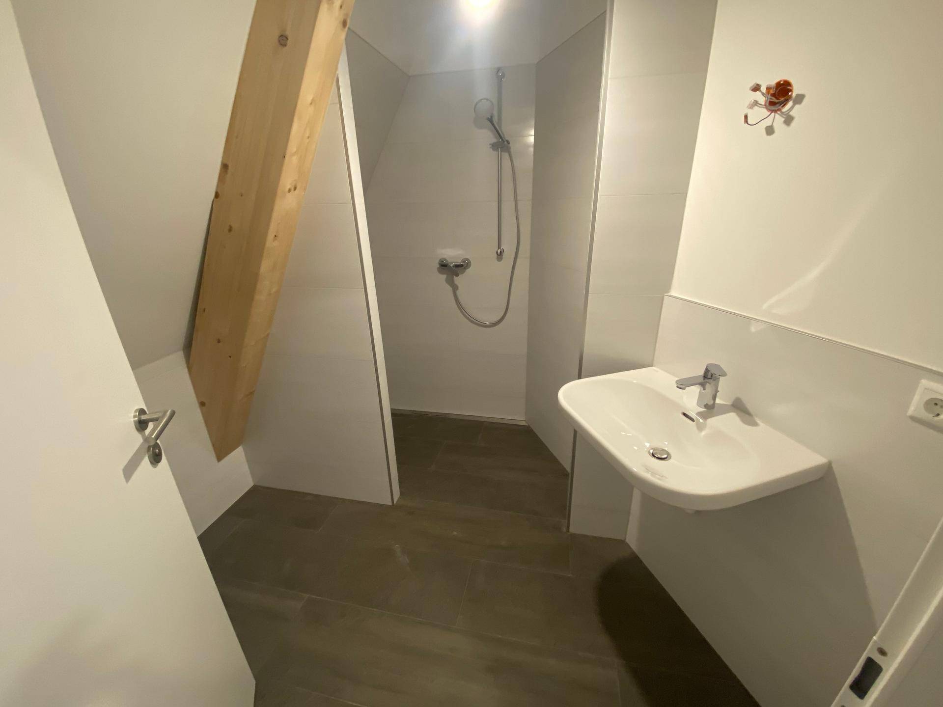 Modernes Badezimmer im Dachgeschoss mit Dusche, Waschbecken und sichtbarem Holzbalken unter der Schräge.
