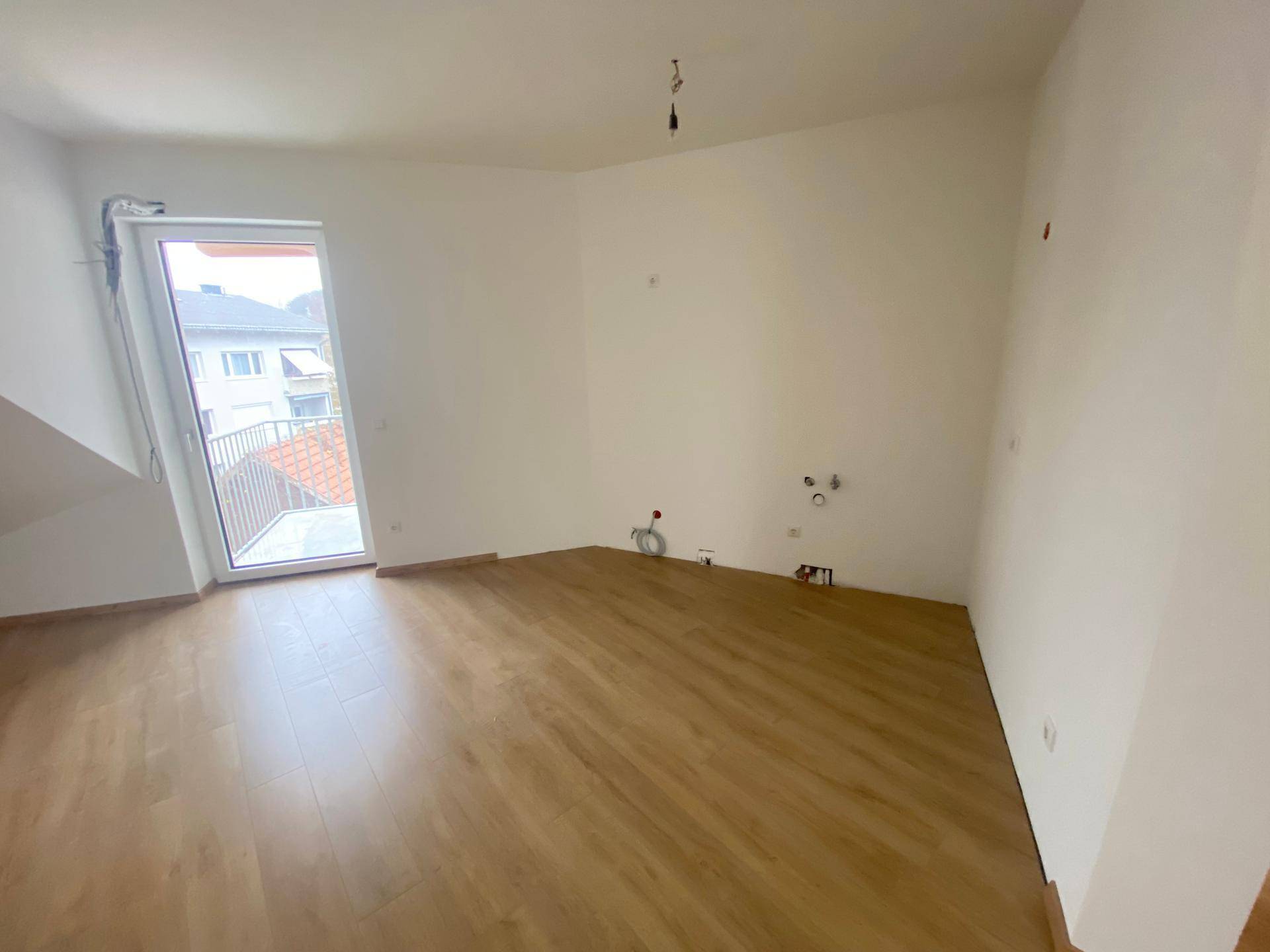 Leerer Raum im Dachgeschoss mit Laminatboden und Anschlüssen für eine Küche, mit Balkonzugang.