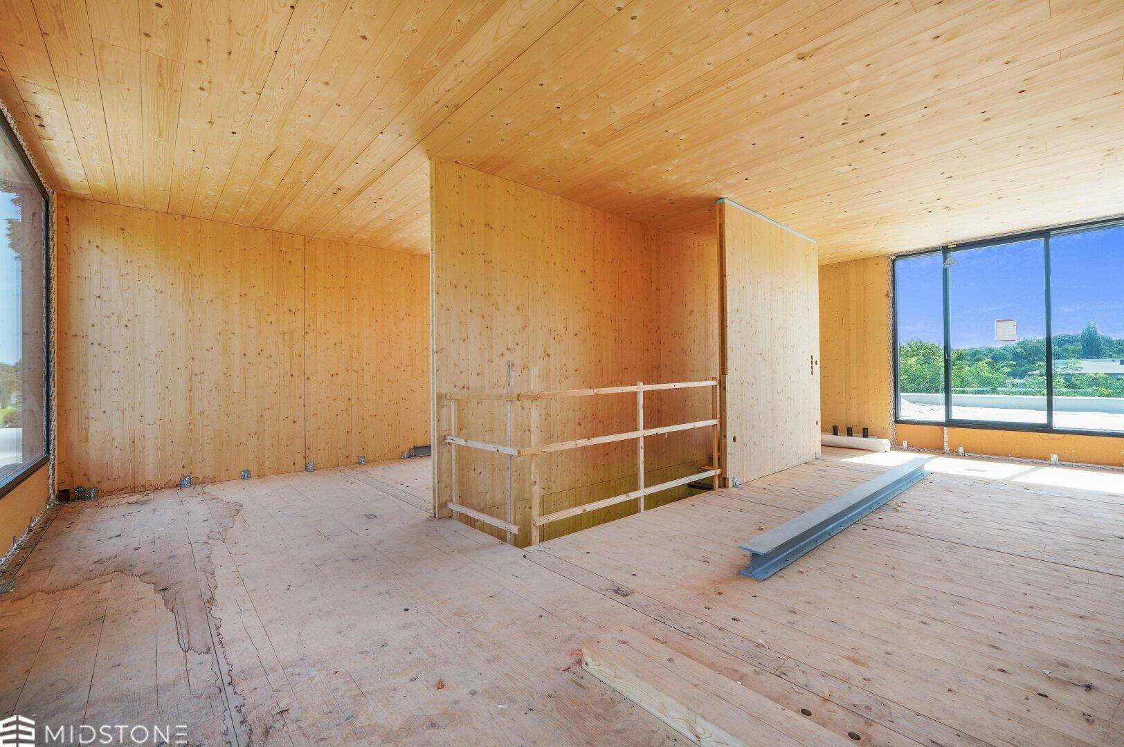 Innenraum im Rohbau mit Holzverkleidung an Wänden und Decke sowie großen Fensterfronten.