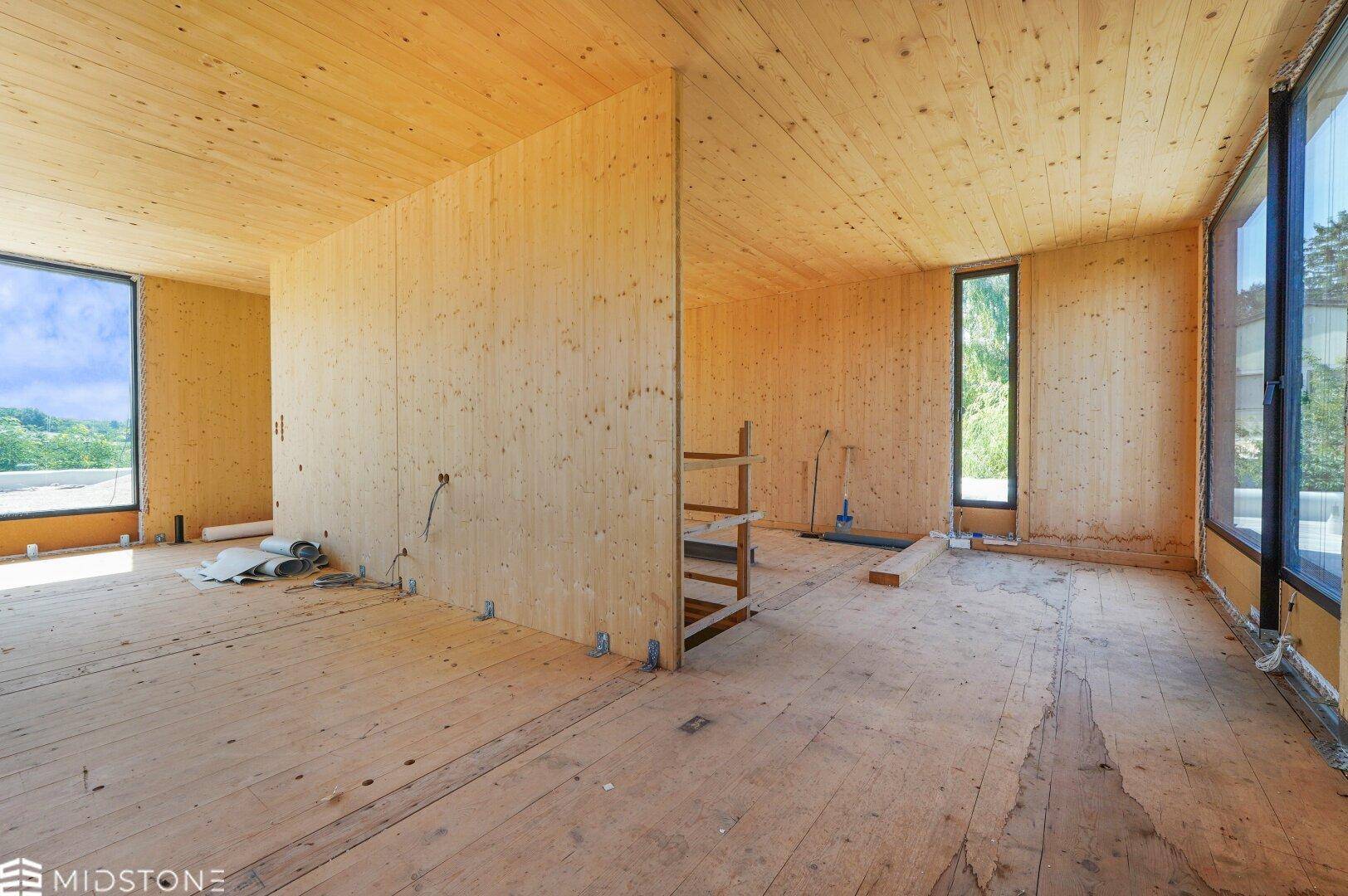 Offener Rohbau mit Holzverkleidung, großen Fenstern und Blick auf die umliegende Landschaft.