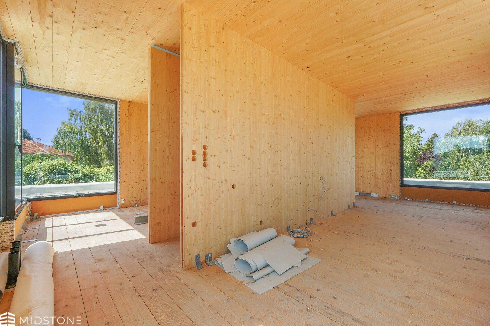 Geräumiger Rohbau mit Holzverkleidung, großen Fenstern und viel natürlichem Lichteinfall.
