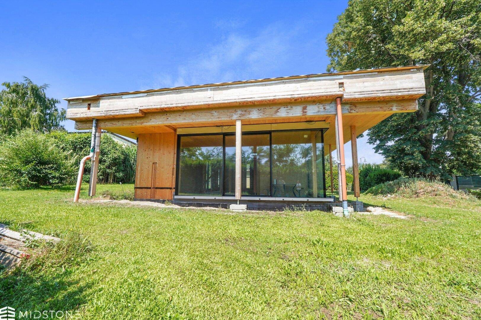 Frontansicht des Neubaus in Holzbauweise mit breiten Fensterfronten und umgebender Grünfläche.