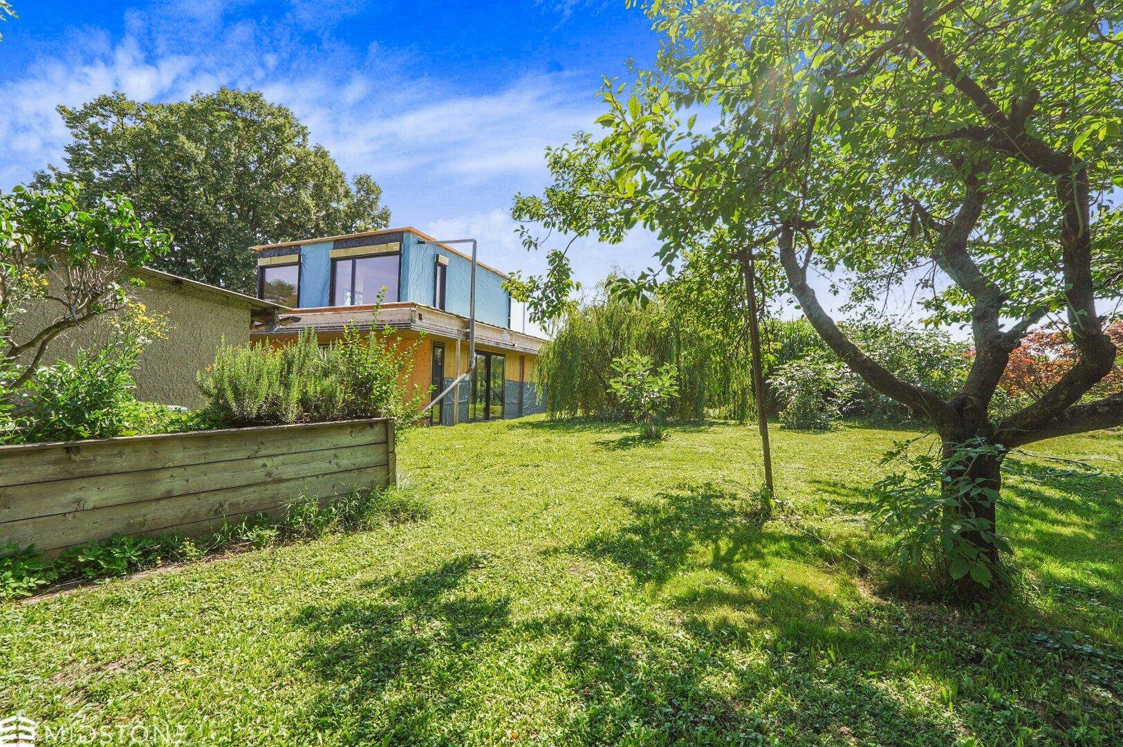 Weitläufiger Gartenbereich mit Bäumen und Blick auf das moderne Holzhaus im Hintergrund.