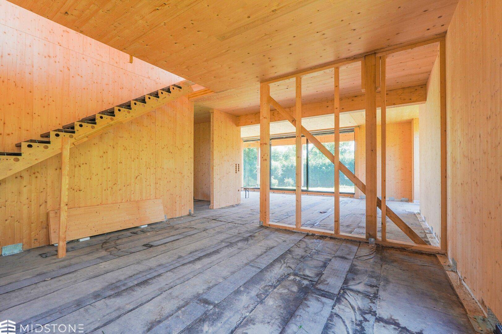 Unfertiger Innenraum in Holzbauweise mit sichtbaren Holzwänden, Decken und einer Treppe.