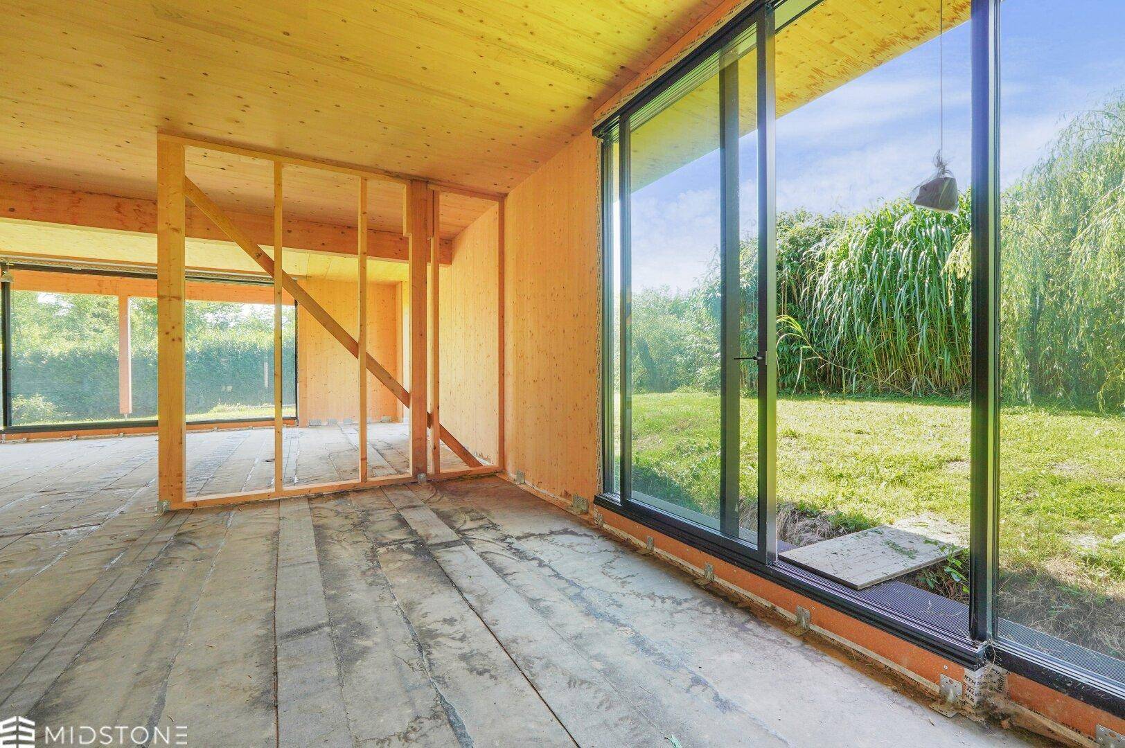 Heller Innenraum in Holzbauweise mit großen Fensterfronten und Blick in den Garten.