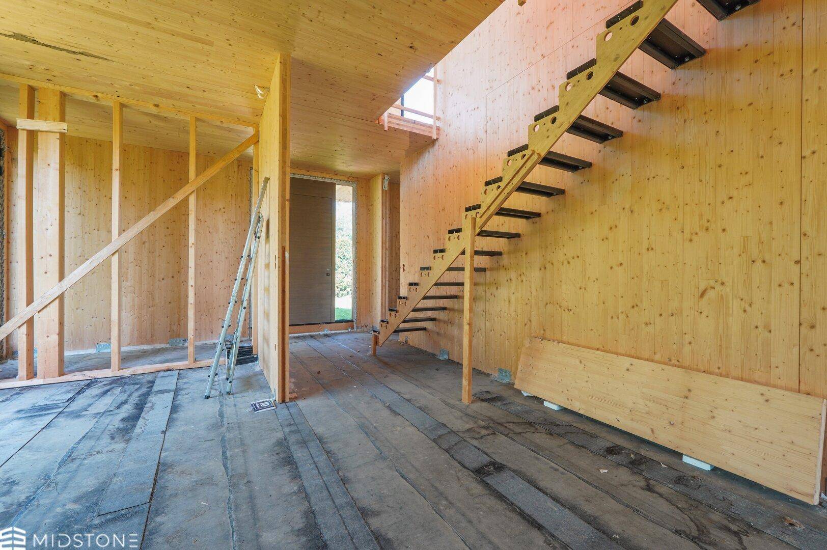 Eingangsbereich des Holzhauses mit offener Treppe und sichtbaren Holzoberflächen.