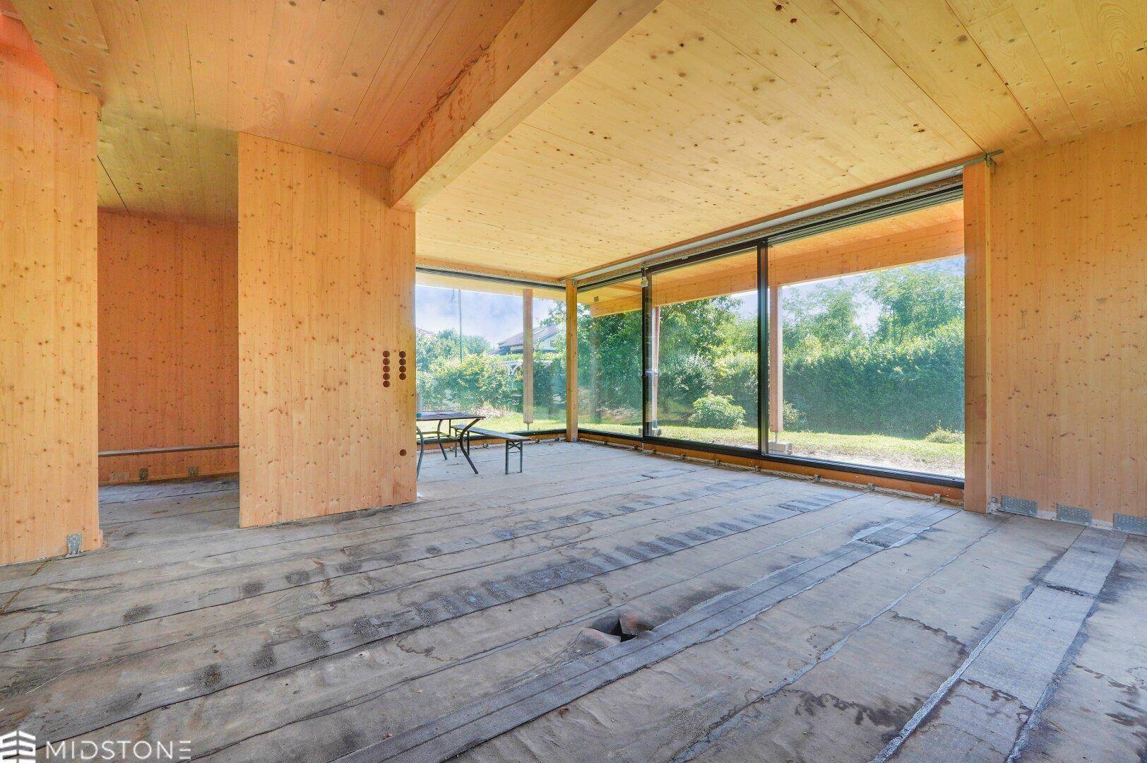 Geräumiger Innenraum in Holzbauweise mit großen Fensterfronten und Blick ins Grüne.