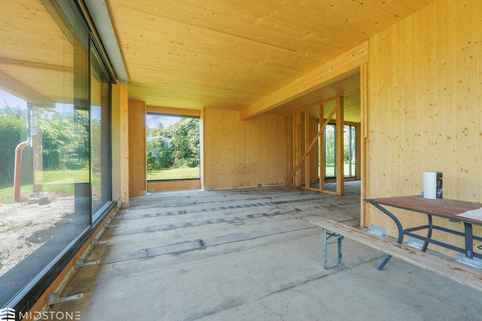 Heller Innenraum in Holzbauweise mit großen Fenstern und Blick auf die umliegende Natur.