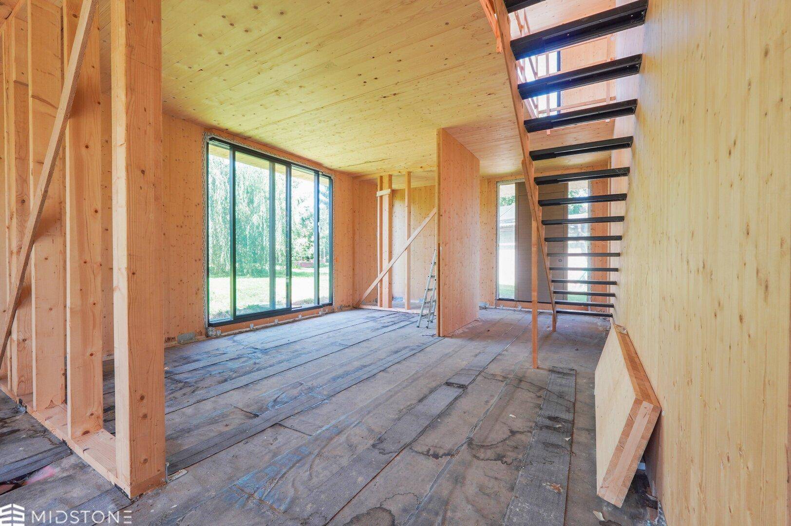 Offener Innenraum in Holzbauweise mit sichtbaren Holzstrukturen und Treppenaufgang.