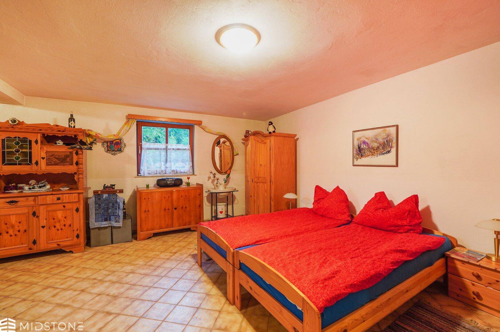 Schlafzimmer mit zwei Einzelbetten, Holzmöbeln und einem Fenster mit Blick ins Grüne.