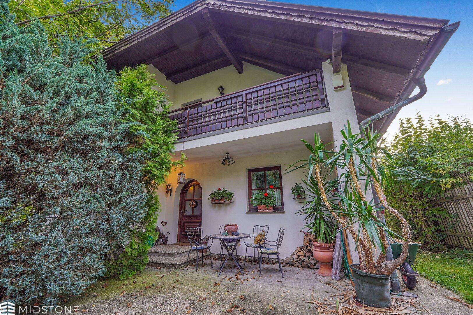 Eingangsbereich mit kleiner Terrasse und Sitzgelegenheiten, umgeben von Pflanzen.
