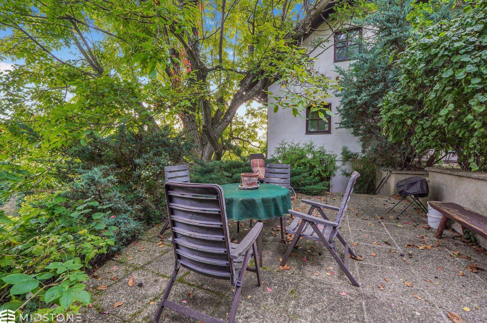 Gemütliche Terrasse mit Gartentisch und Stühlen, umgeben von üppiger Vegetation.