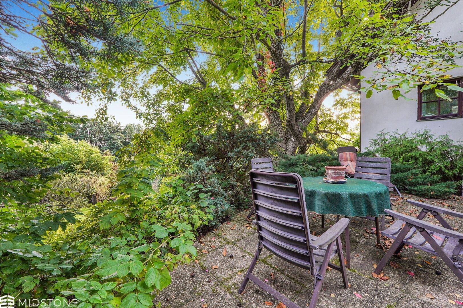 Sitzbereich im Freien auf einer Terrasse, umgeben von Bäumen und Sträuchern.