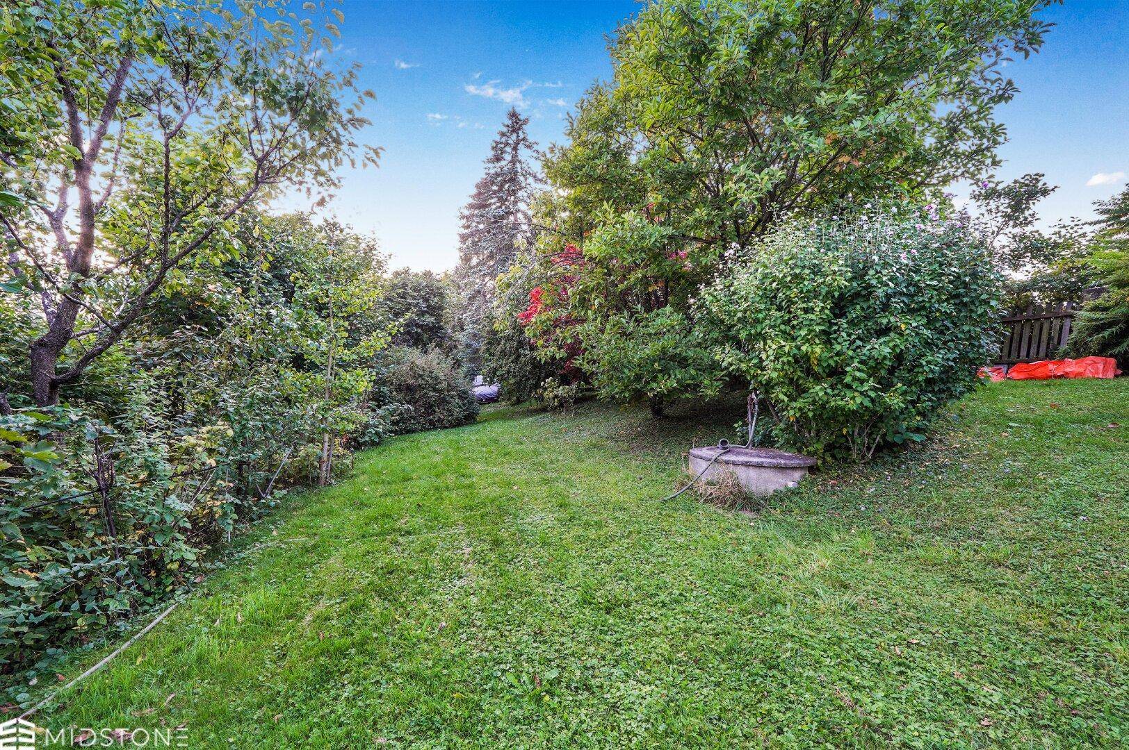 Großer, grüner Garten mit altem Brunnen und vielen Bäumen und Sträuchern.