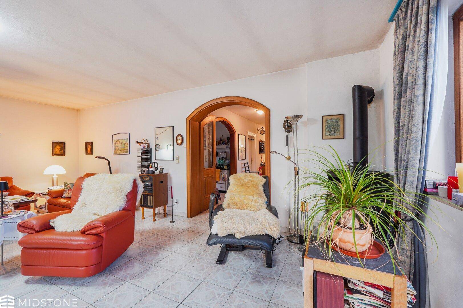 Gemütliches Wohnzimmer mit Kaminofen, roten Ledermöbeln und Fliesenboden.