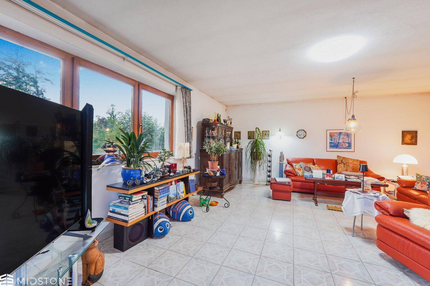 Helles Wohnzimmer mit großen Fenstern, roter Ledercouch und Fliesenboden.