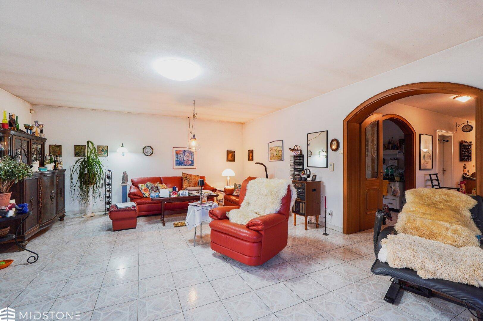 Geräumiges Wohnzimmer mit roten Ledermöbeln, Fliesenboden und traditioneller Einrichtung.