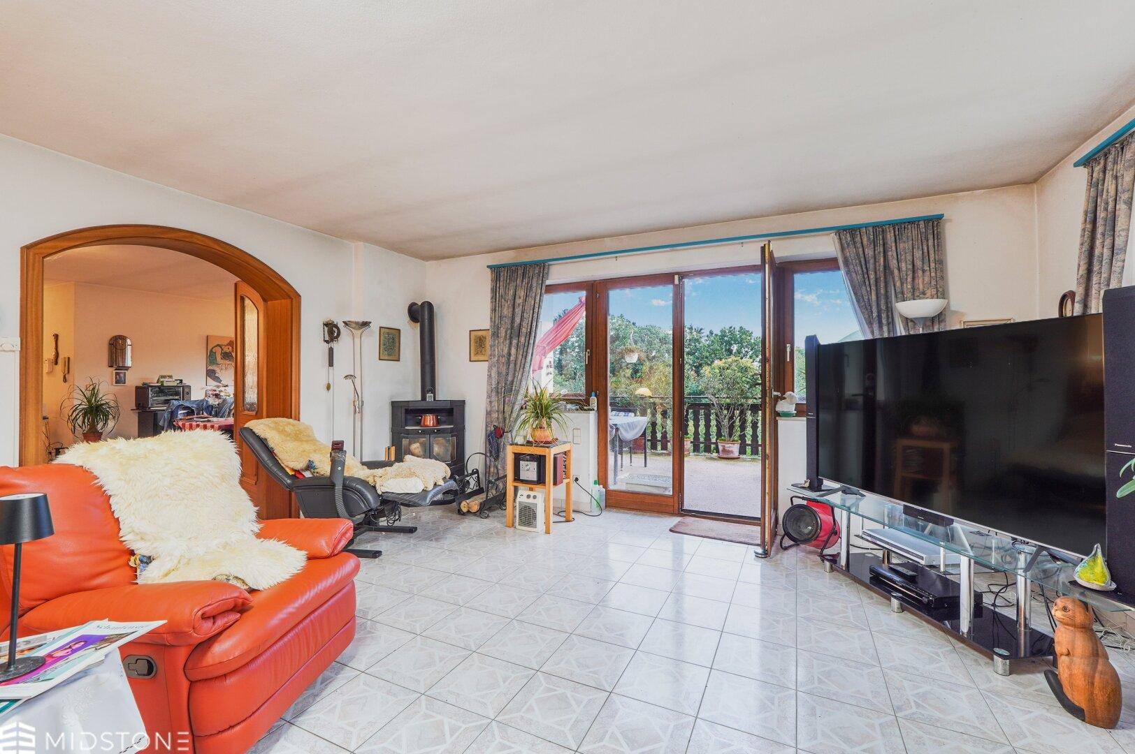 Wohnzimmer mit Zugang zum Balkon, Kaminofen und großem Fernseher.