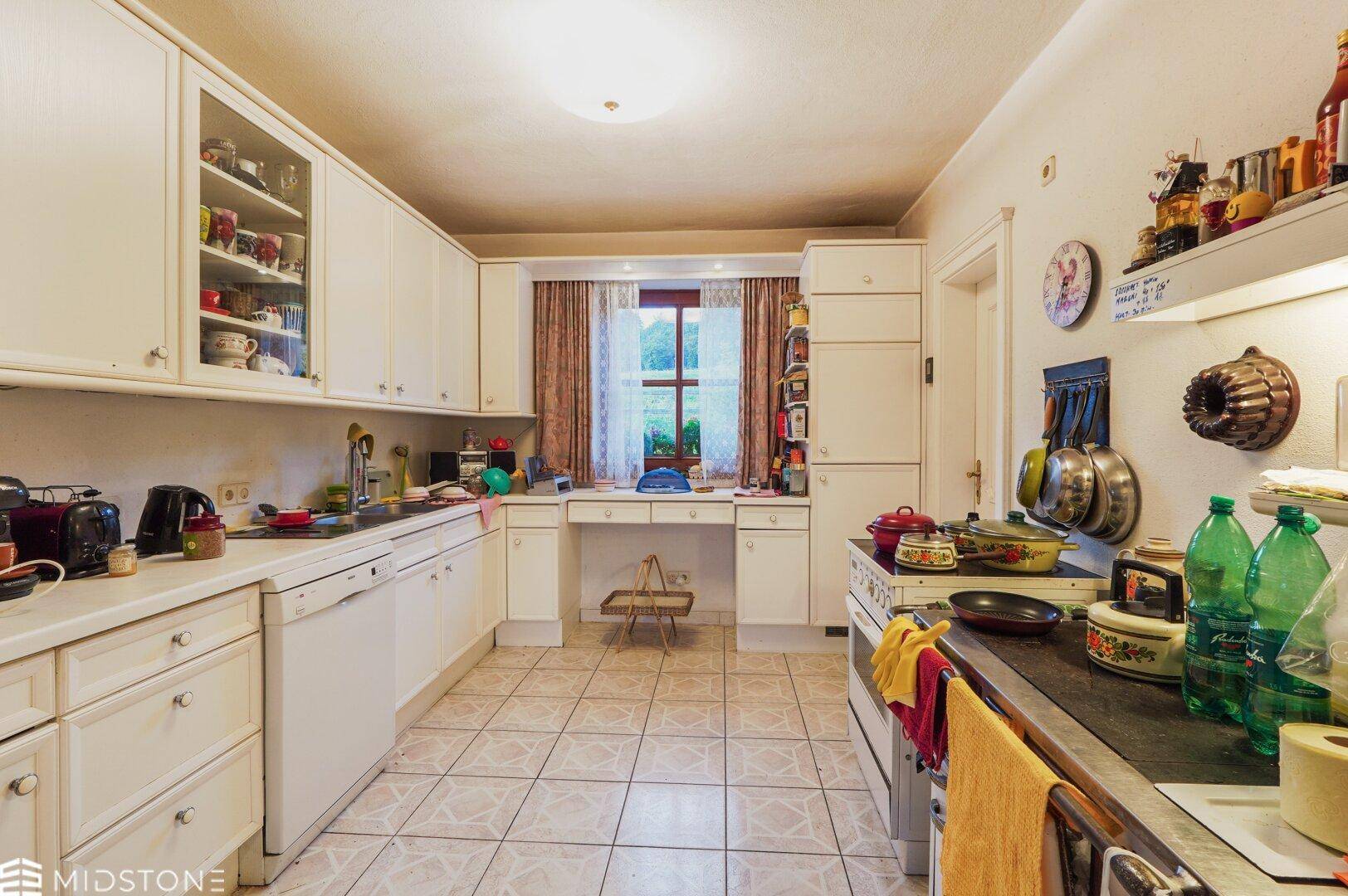 Funktionale Küche mit weißen Einbauschränken, Fliesenboden und Fensterblick.