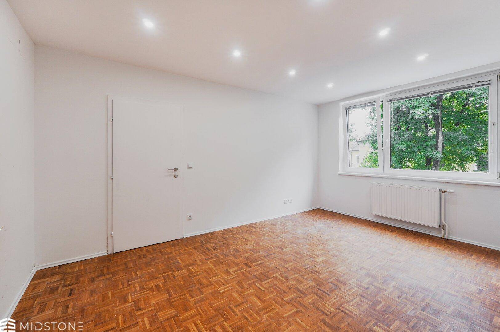 Freundliches Zimmer mit Parkett und Blick ins Grüne, ideal für Wohn- oder Schlafzwecke.