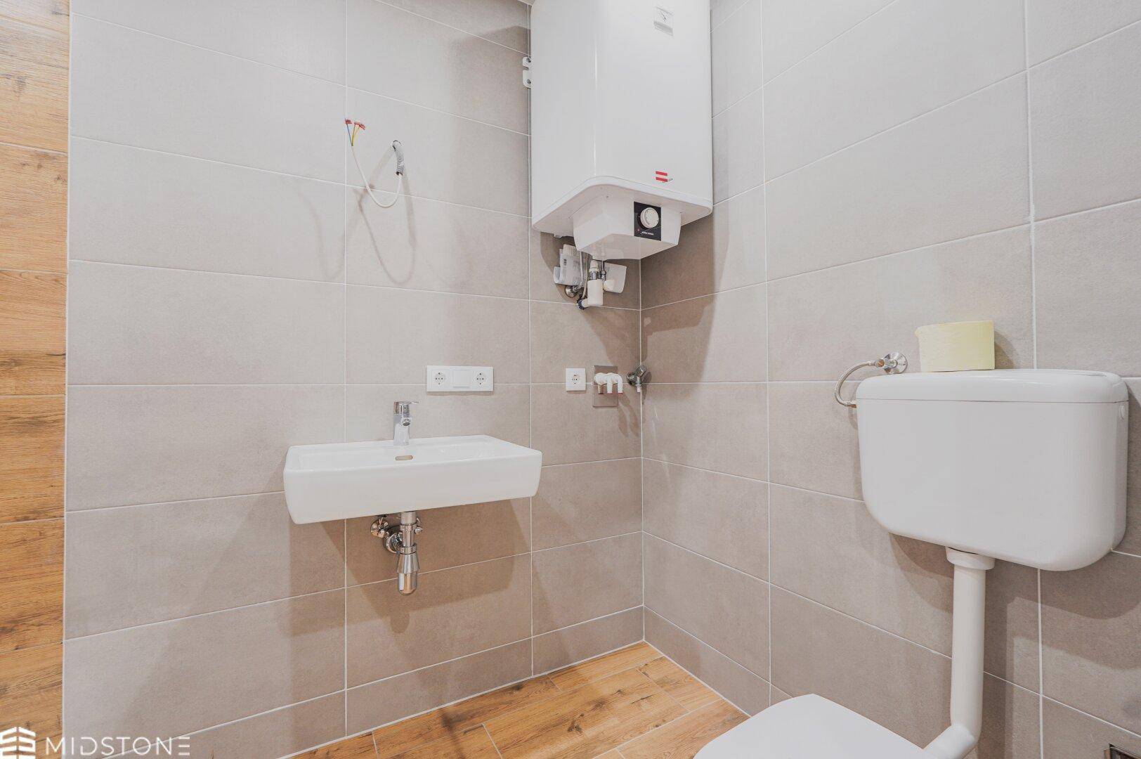 Funktionales Badezimmer mit WC, Waschbecken und Duschbereich, ausgestattet mit modernen Fliesen.