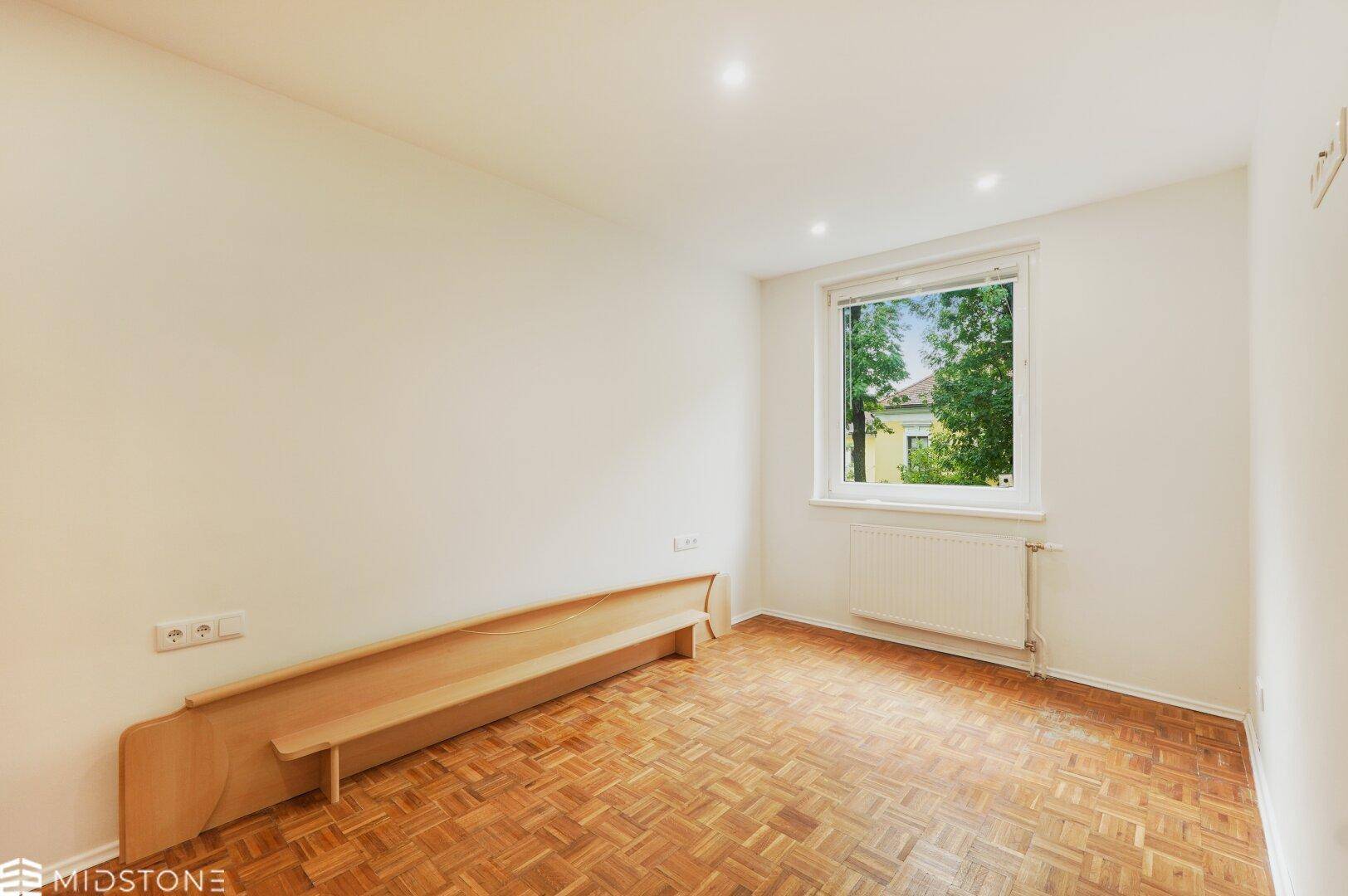 Helles Schlafzimmer mit Parkettboden und großem Fenster, bietet eine ruhige Atmosphäre.
