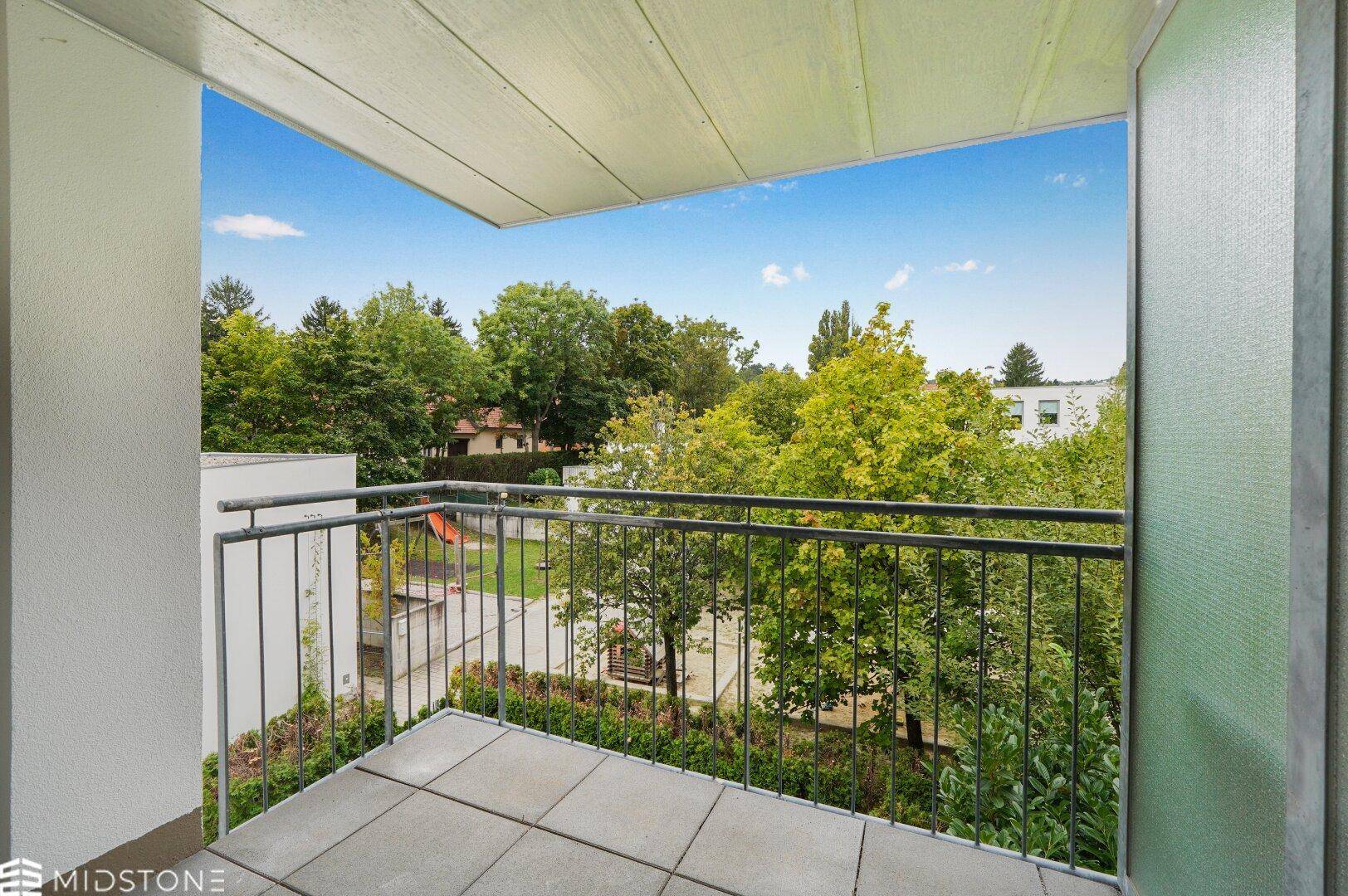 Balkon mit Blick auf einen Spielplatz und grüne Bäume, ideal für Familien.