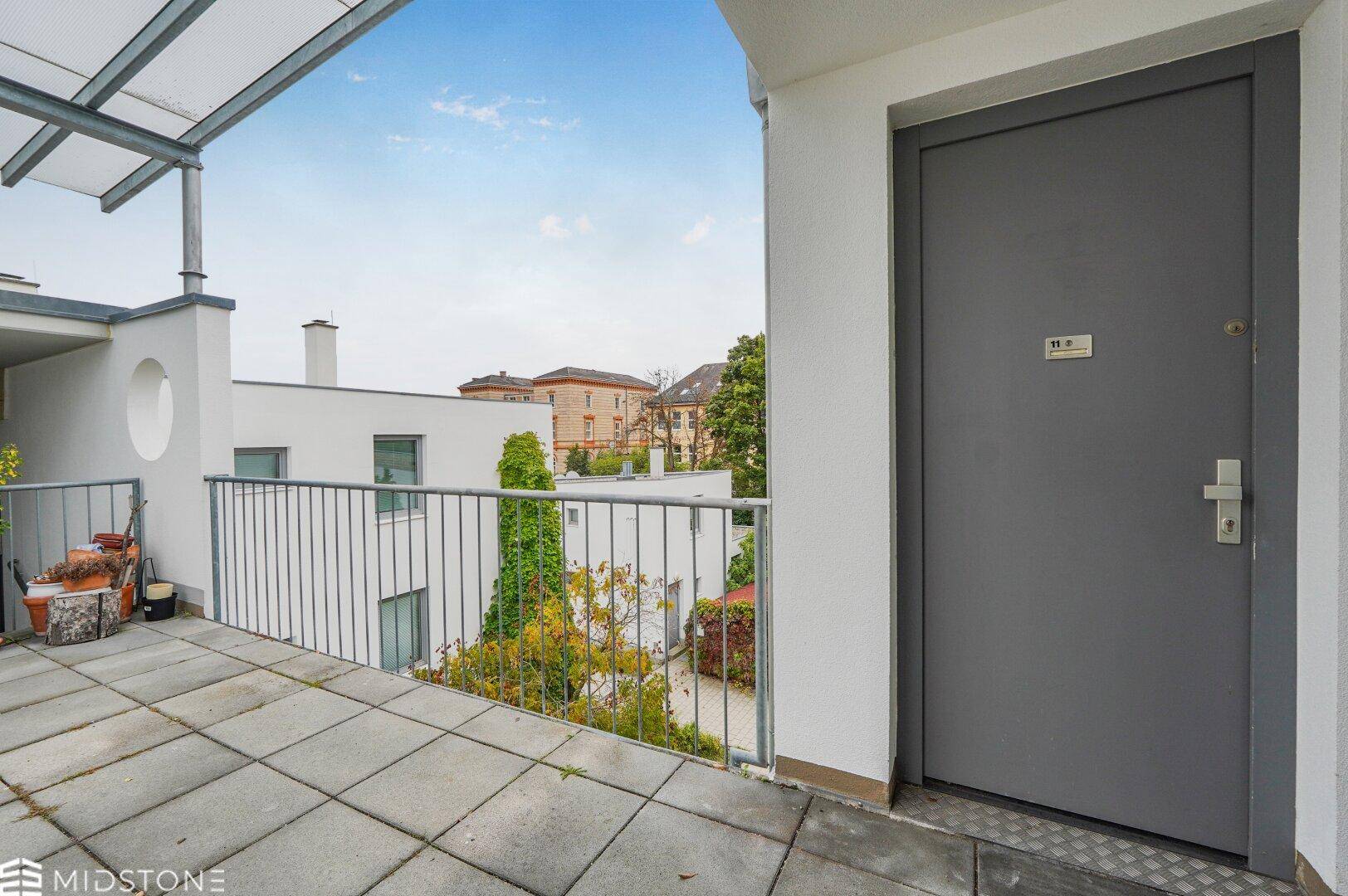 Geräumige Terrasse mit Zugangstür und Blick auf die umliegenden Gebäude.