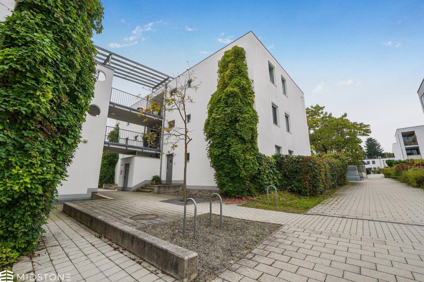 Moderne Wohngebäude mit weißer Fassade, umgeben von viel Grün und Fahrradständern.