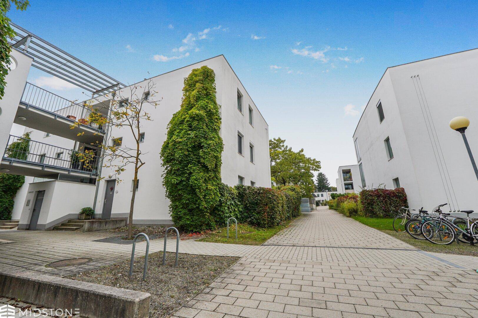 Außenansicht der modernen Wohnanlage mit gepflastertem Weg und begrünten Bereichen.