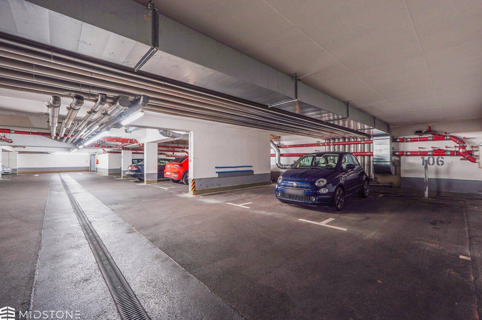 Tiefgarage mit mehreren Stellplätzen und sichtbaren Lüftungsrohren an der Decke.