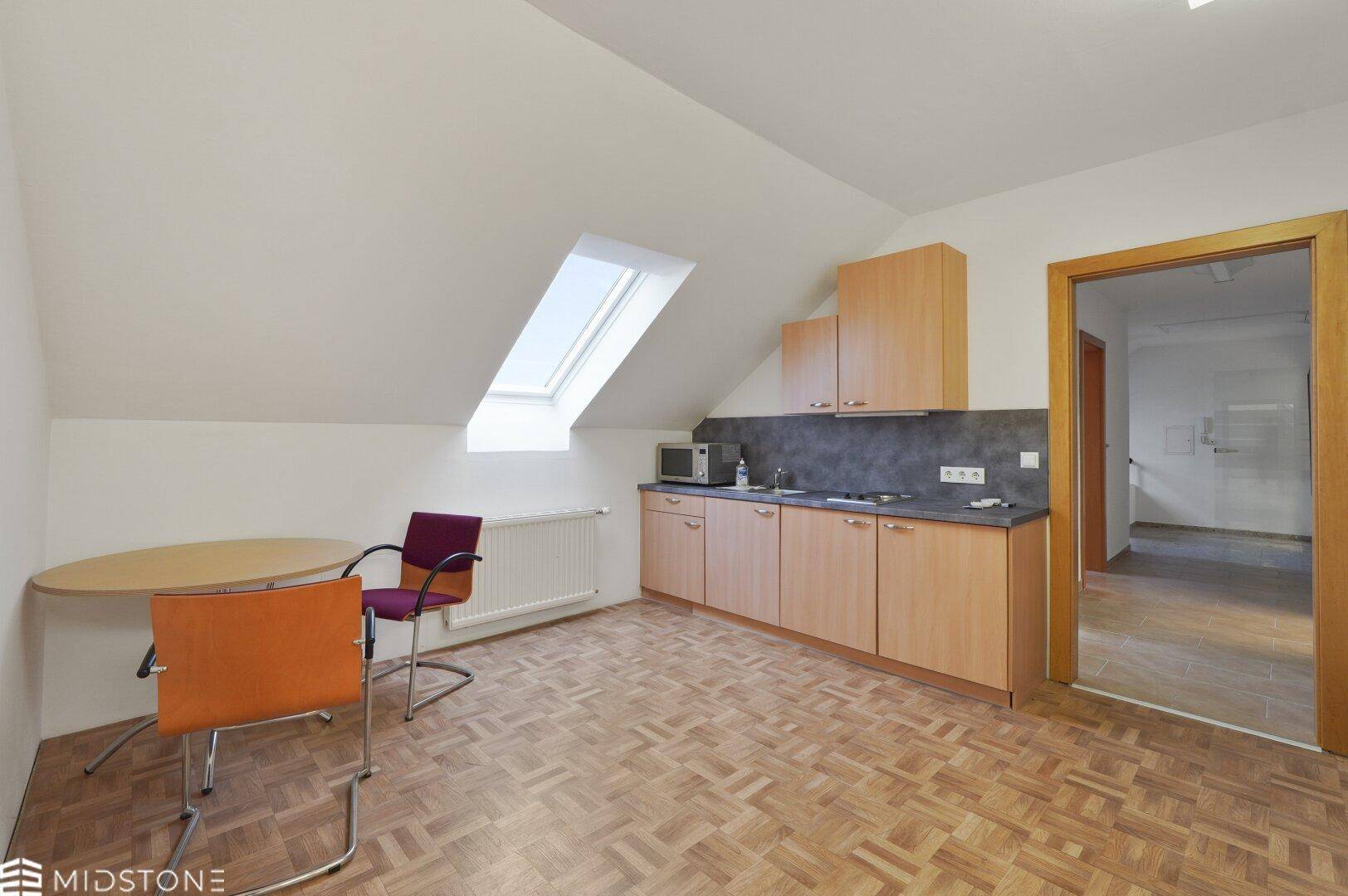 Funktionale Küchenzeile im Dachgeschoss mit Dachfenster, Mikrowelle und Essbereich, ideal für Pausen.