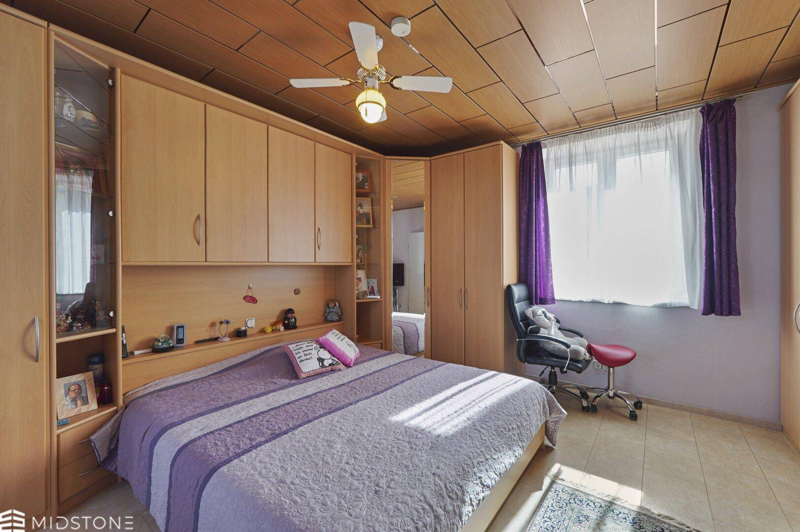 Gemütliches Schlafzimmer mit Einbauschränken, Deckenventilator und lila Bettwäsche.