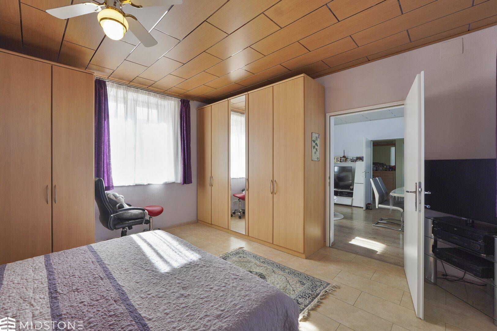 Schlafzimmer mit Holzdecke, Einbauschränken und Zugang zu einem weiteren Raum.