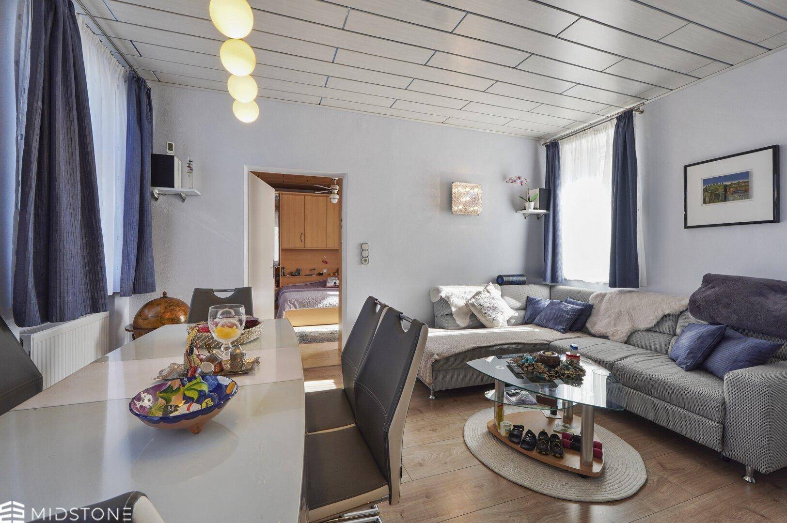 Wohn- und Essbereich mit hellem Holzboden und Zugang zu einem weiteren Zimmer.