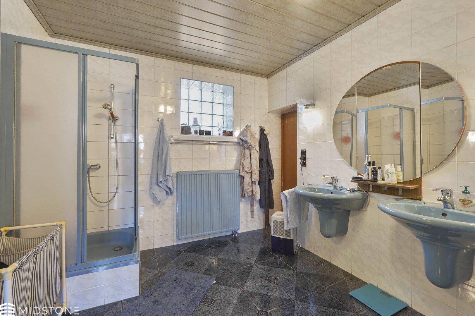 Badezimmer mit zwei Waschbecken, Duschkabine und blauen Fliesen.