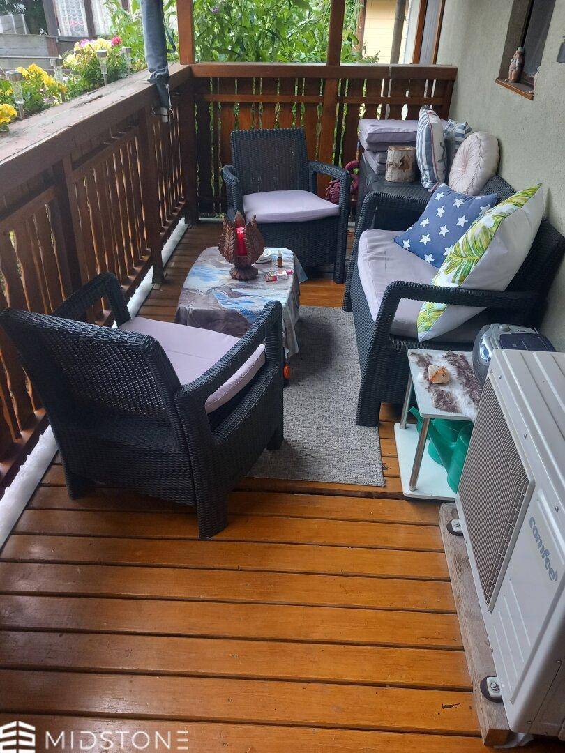 Balkon mit Holzfußboden, bequemen Sitzmöbeln und Klimaanlage-Außengerät.