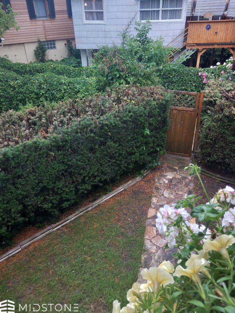 Gepflegter Gartenbereich mit Hecken, Rasenfläche und einem kleinen Holztor.