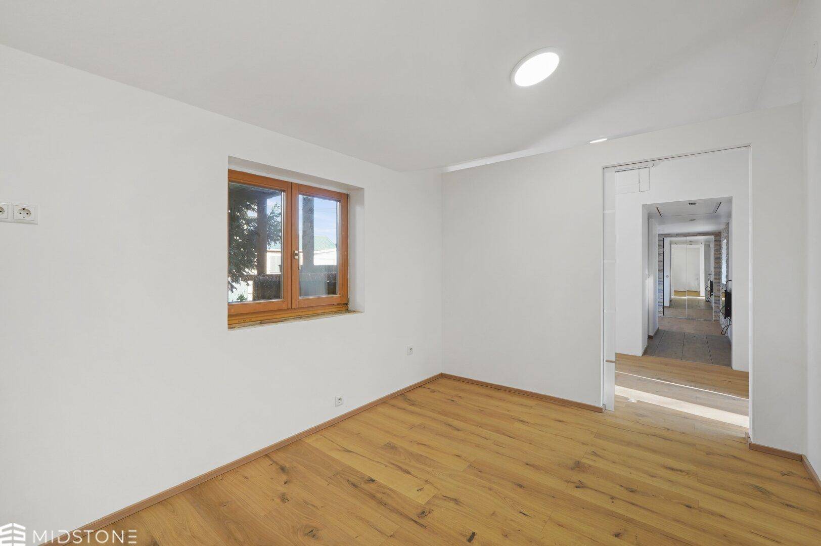 Helles Zimmer mit Holzboden und Zugang zu einem Flur, ideal als Schlafzimmer.