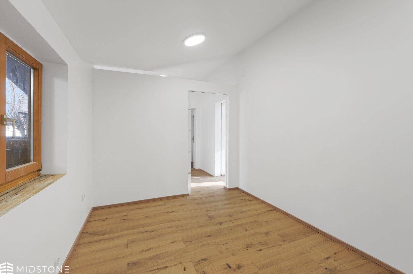 Geräumiges Zimmer mit Holzboden, weißen Wänden und viel Tageslicht.