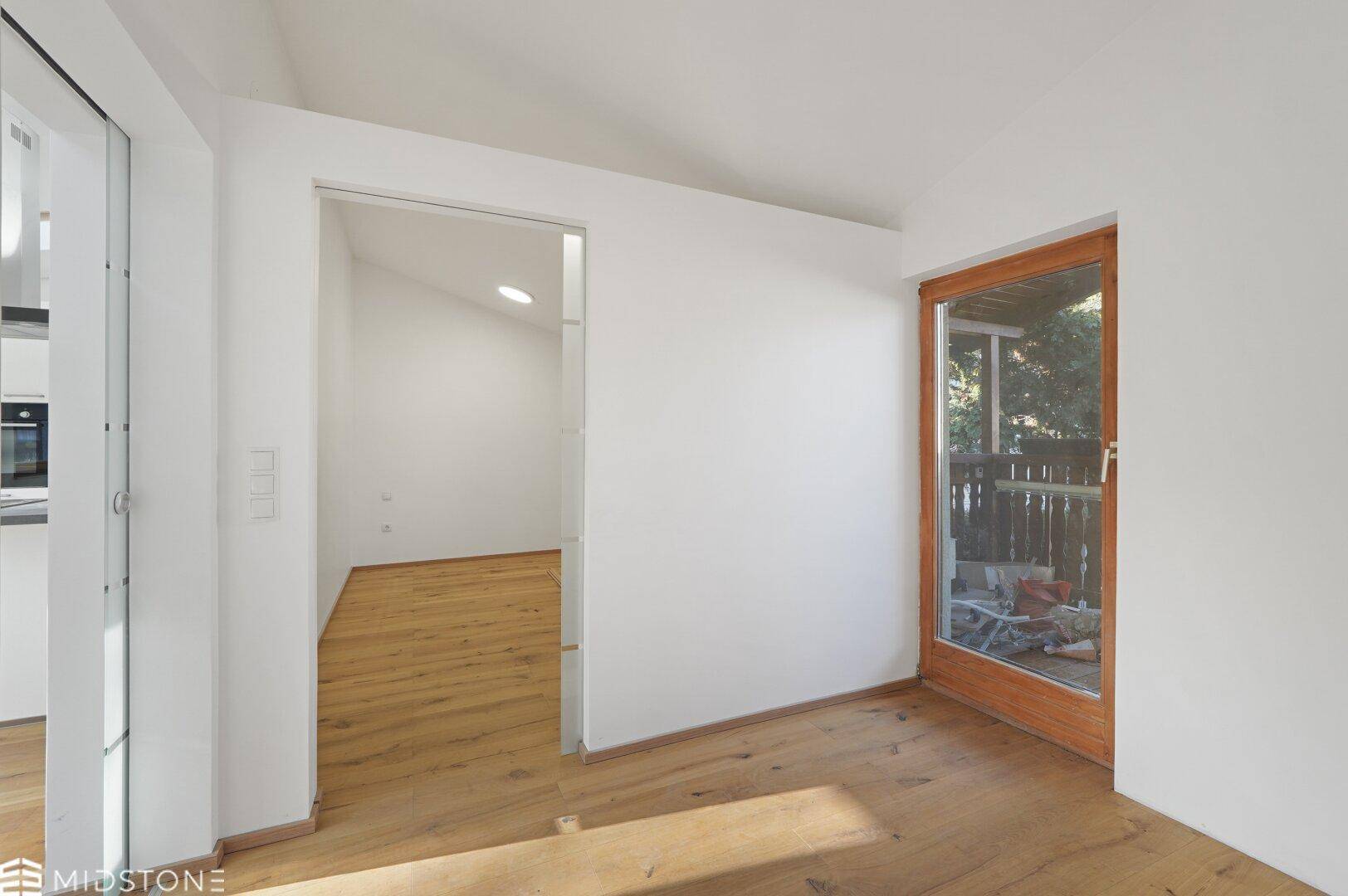 Heller Raum mit Holzboden und Zugang zu einem Balkon oder einer Terrasse.