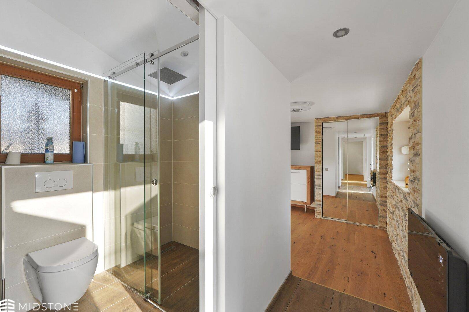 Modernes Badezimmer mit begehbarer Dusche und Zugang zu einem hellen Flur.