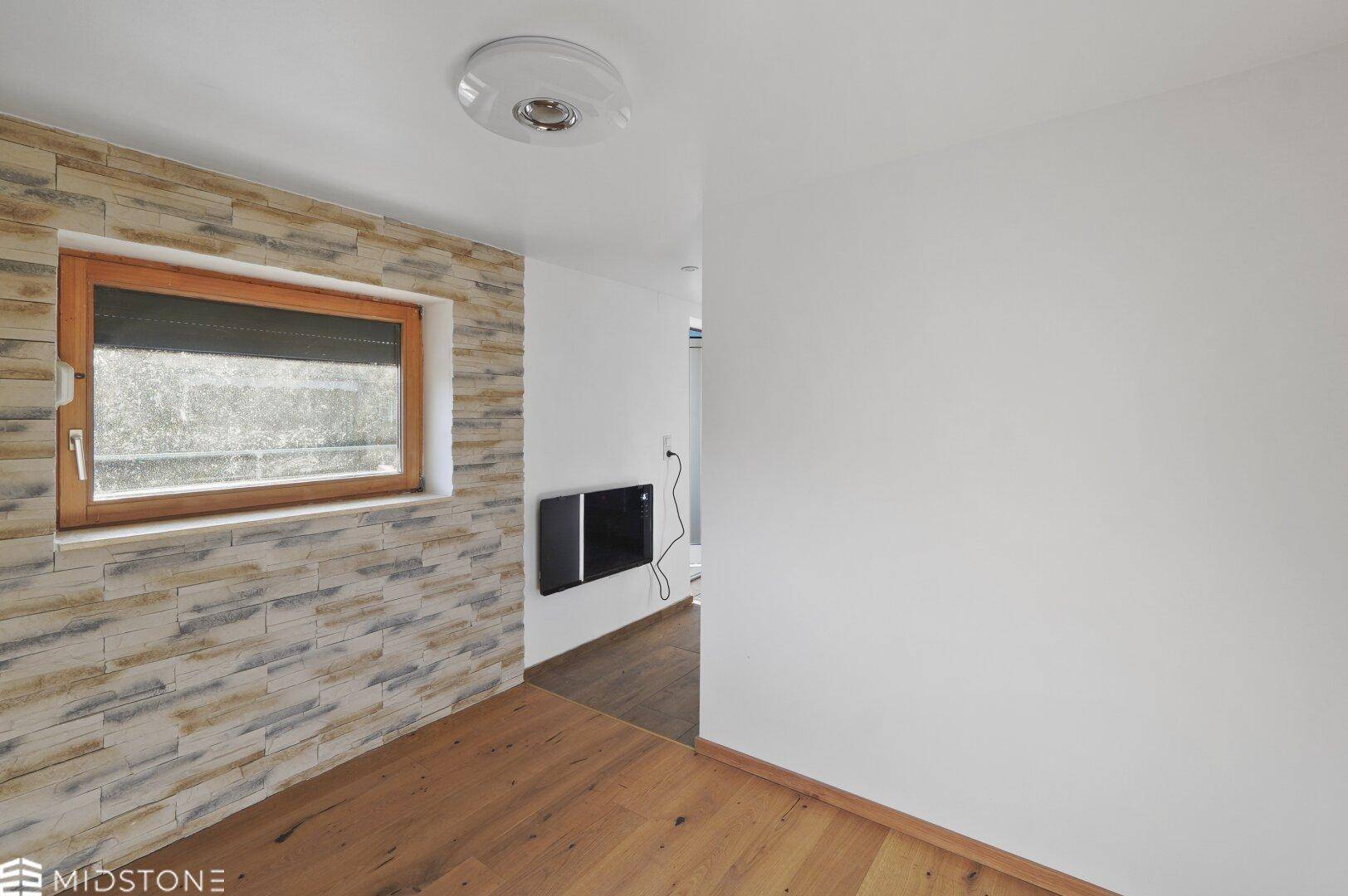 Heller Flur mit dekorativer Steinwand und Fenster mit Rollladen.